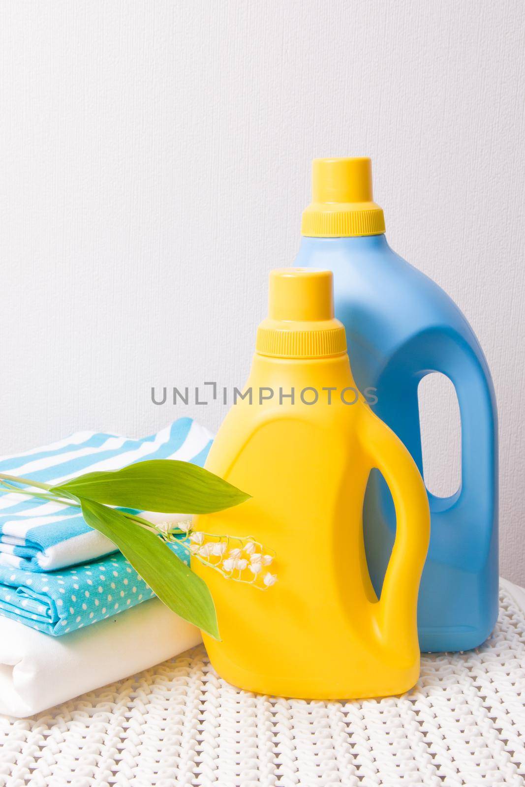 colored fabric clothes, lily of the valley flower, washing gel and fabric softener on a captive basket, yellow and blue bottles for gel without labels
