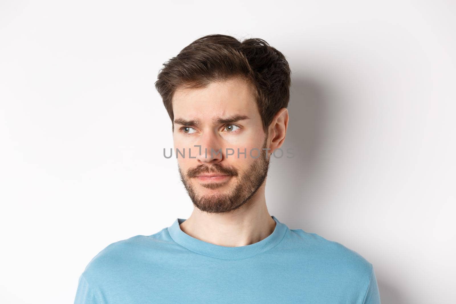 Close-up of disappointed sad man, grimacing and frowning, looking left upset, standing doubtful against white background by Benzoix