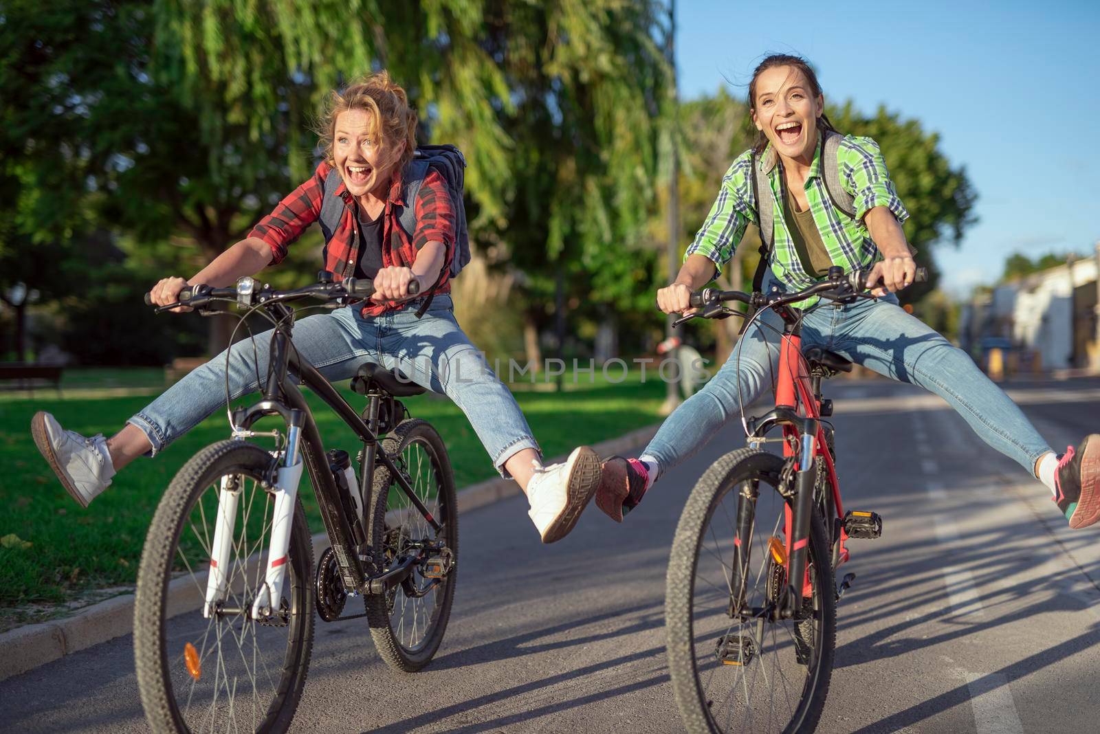 Two pretty young caucasian girls having fun on bicycles along the street. Best friends enjoying a day on bikes. Sunny summer evening.