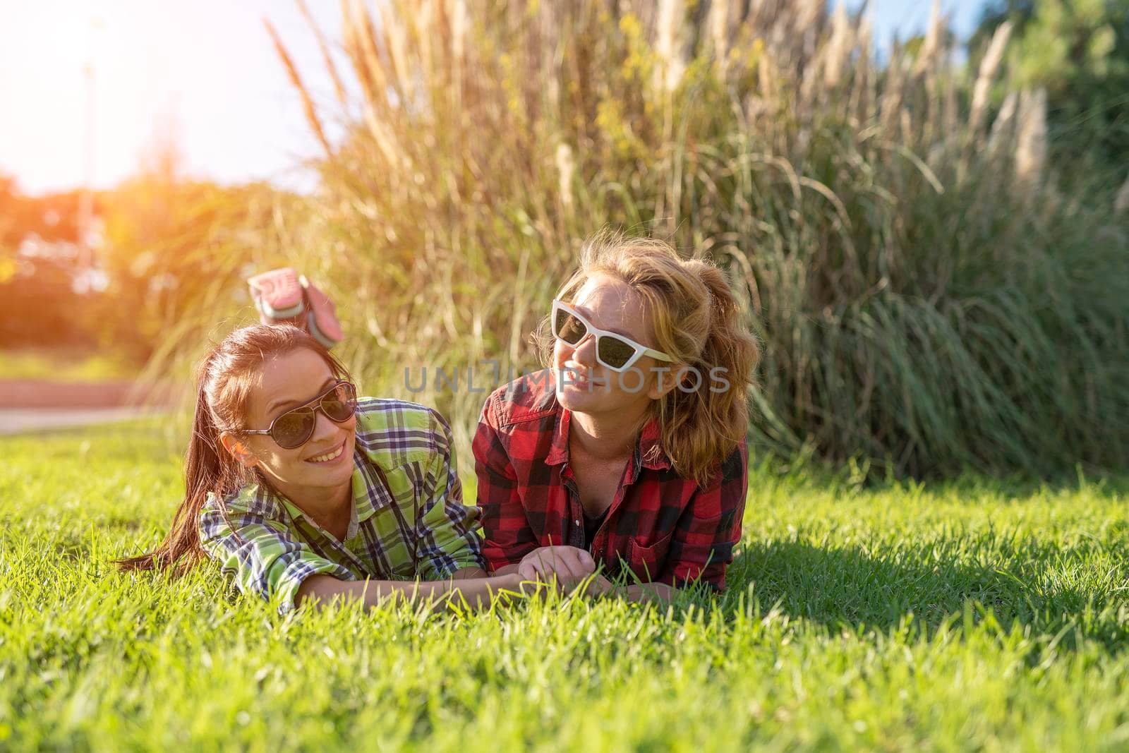 two young pretty teenager girls best friends laying on grass at sunny summer day.