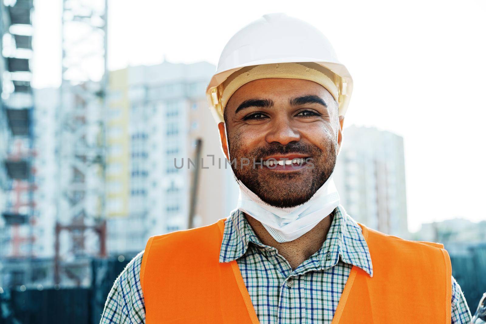 Portrait of mixed race man builder in workwear and hardhat wearing medical mask, close up photo