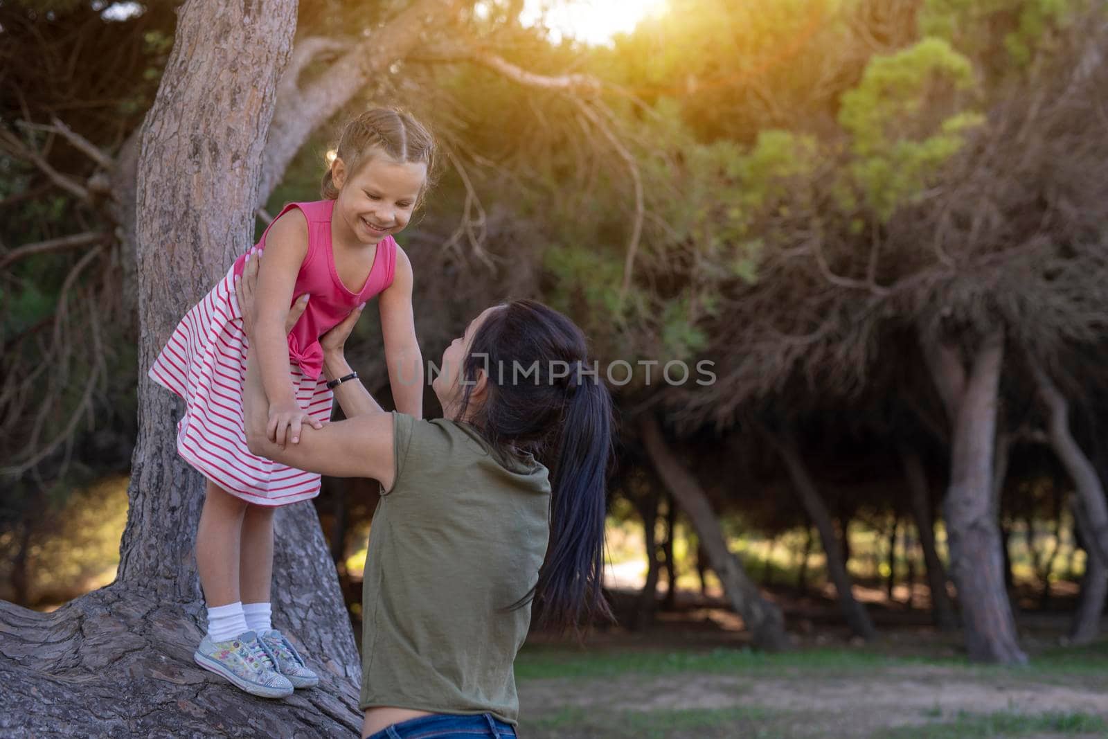 Beautiful mother and her little daughter outdoors. Beauty Mum and her Child playing in Park together at sunset. Outdoor Portrait of happy family. Mother's Day.