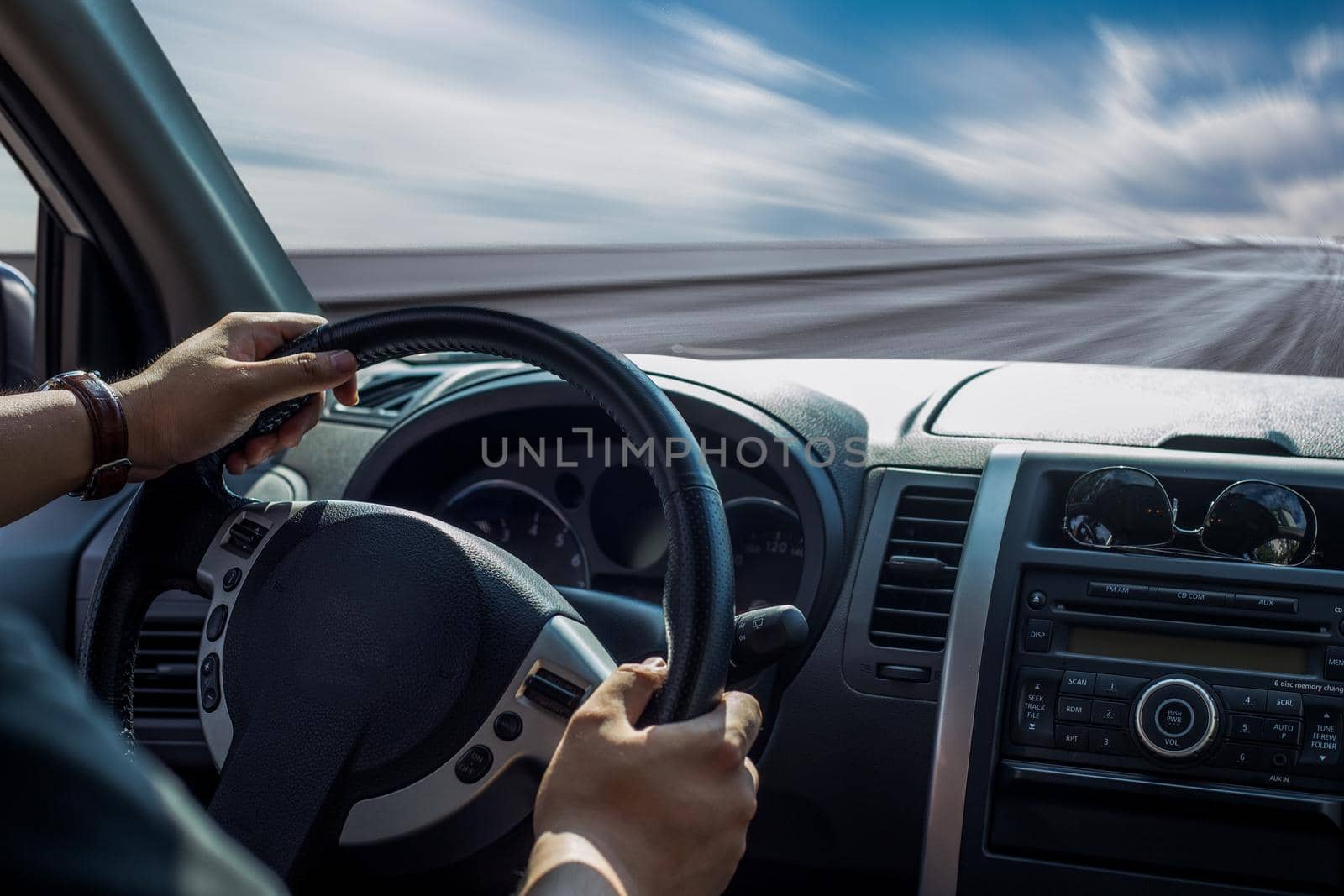 Hands of a driver on steering wheel of a car and empty asphalt road