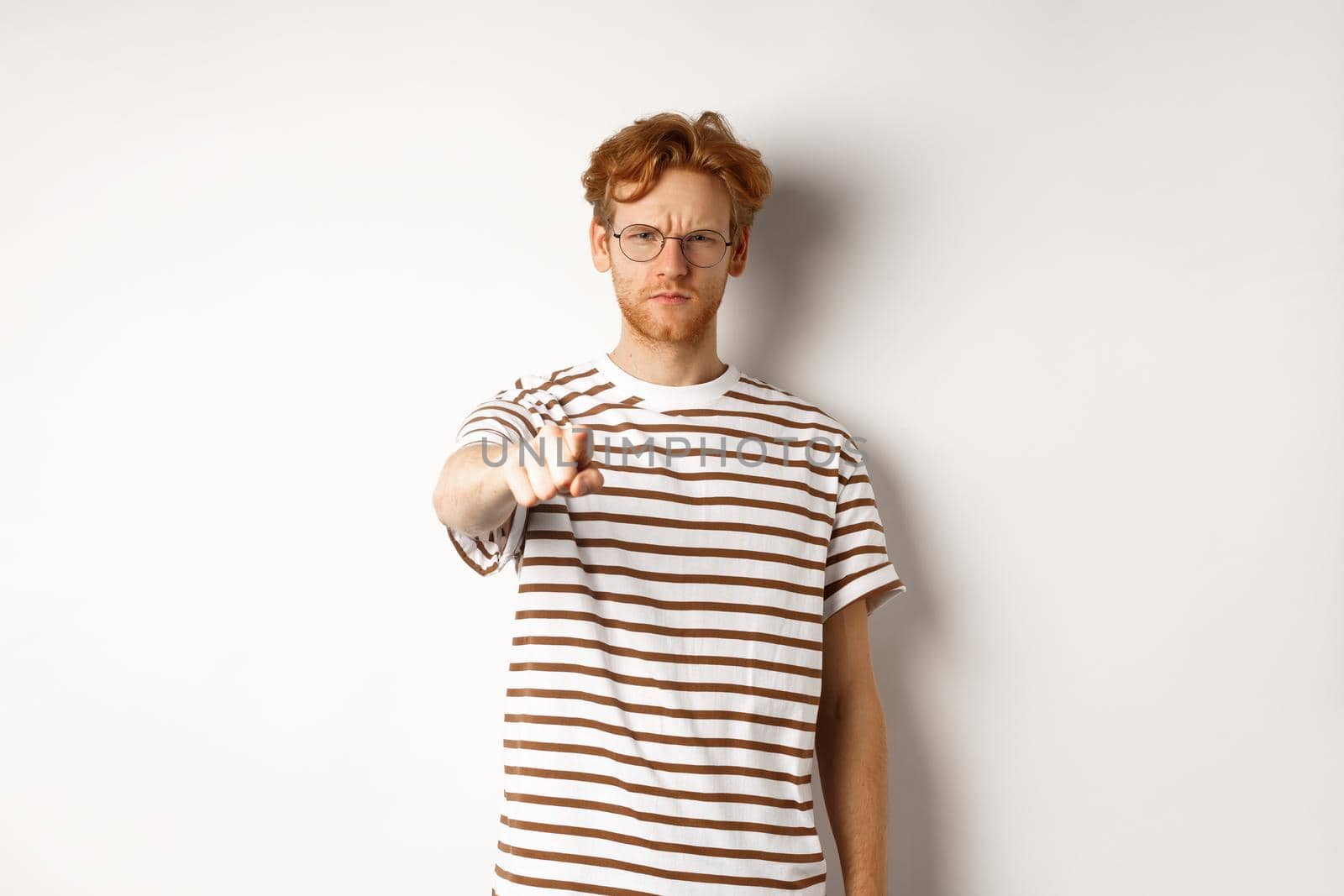 Angry and serious guy with red hair accusing you, frowning and pointing finger at camera, blame someone, standing over white background by Benzoix