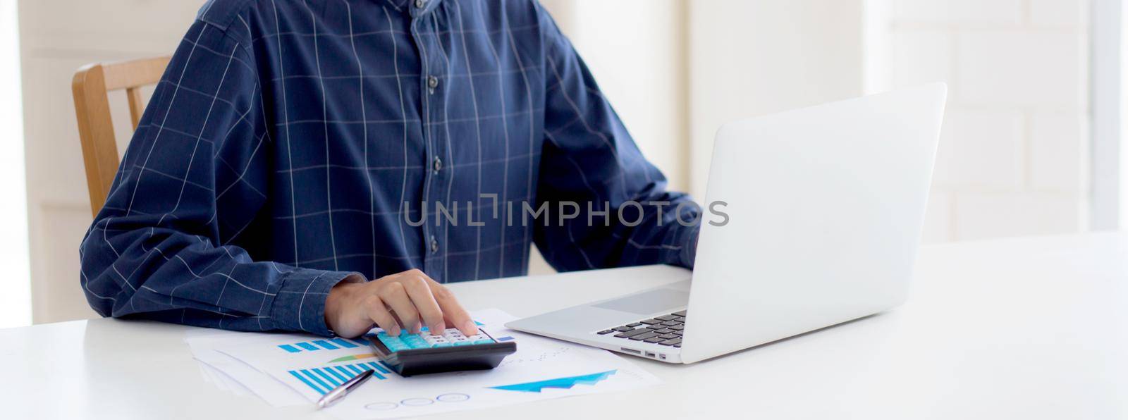 Young asian business man working using calculator for planning accountant, graph for finance and report statistics, investment and profit of income, businessman analyzing expenses with chart.