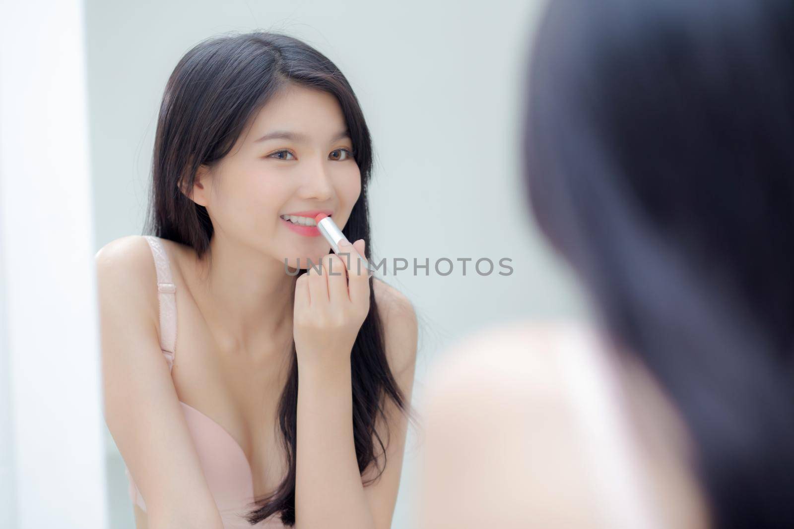 Beautiful young asian woman applying lipstick pink with style bright and shiny on mouth, beauty girl looking mirror for makeup cosmetic with lip elegance, fashion make up with luxury and sexy.