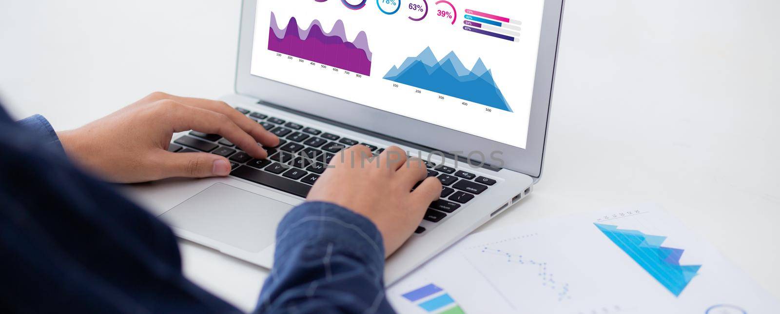 Young asian business man working laptop computer blank display screen while report graph and chart paper on desk, businessman analysis statistic of finance on table, planning for success, indoor.