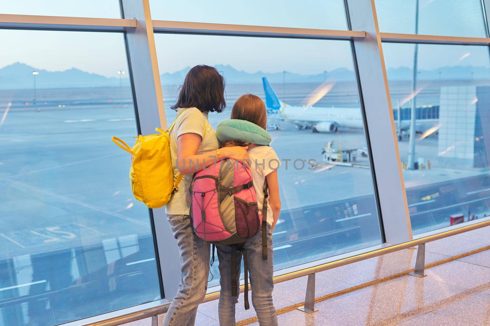 Airport passengers family mother and daughter child looking at planes in panoramic window by VH-studio