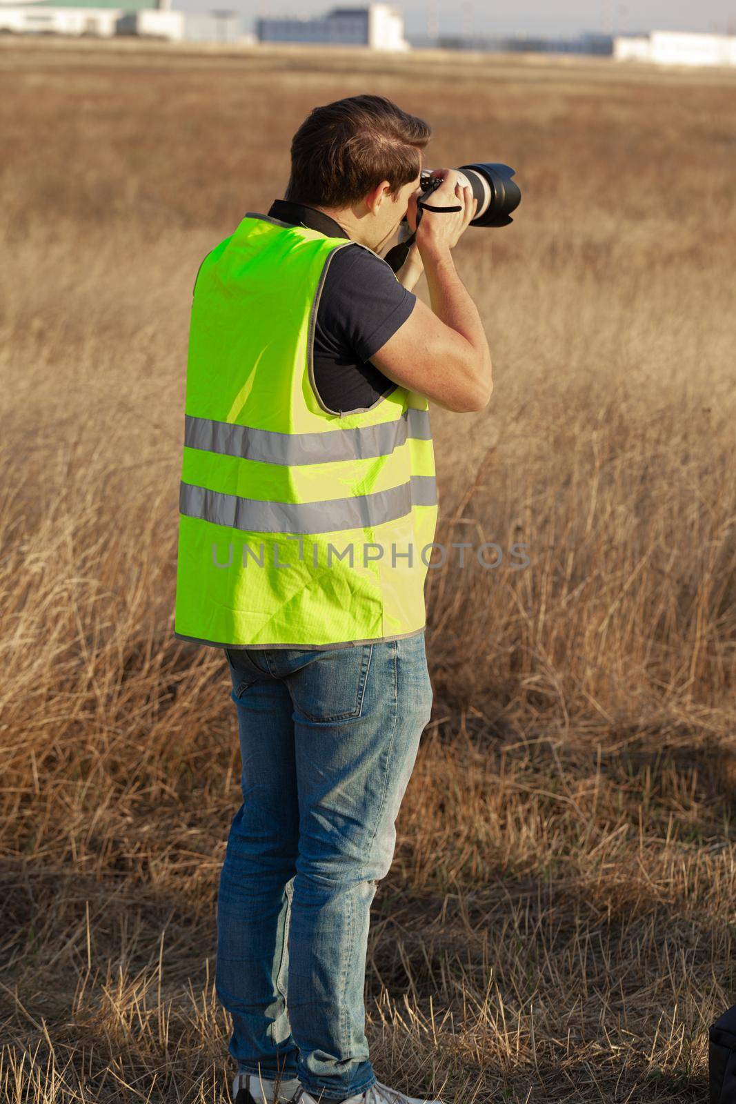 Man in yellow vest does plane spotting at the airport by Fabrikasimf