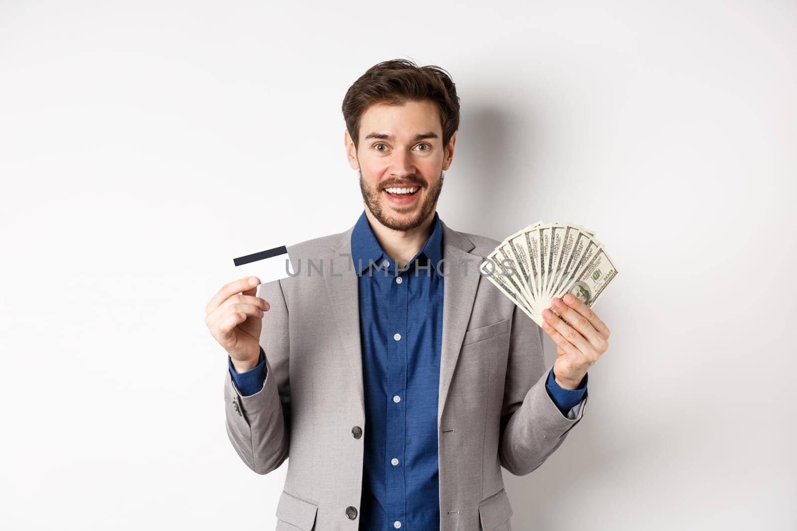 Happy successful businessman in suit showing money and credit card, smiling at camera, white background by Benzoix