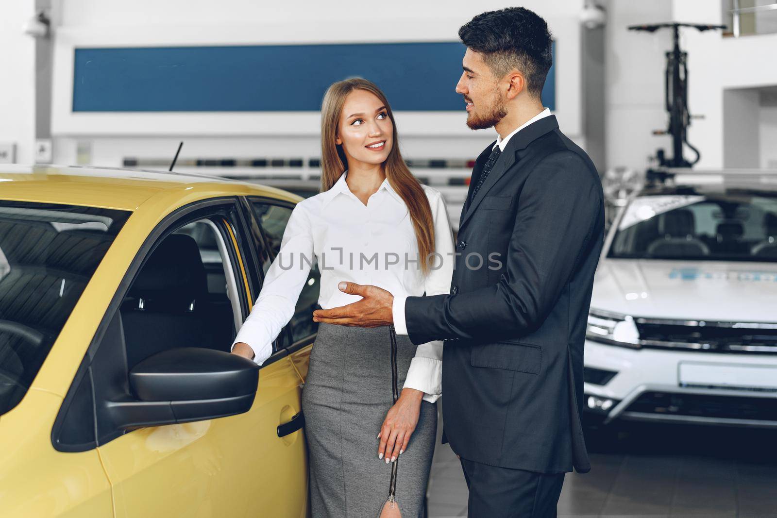 Man car dealer showing a woman buyer a new car in car salon