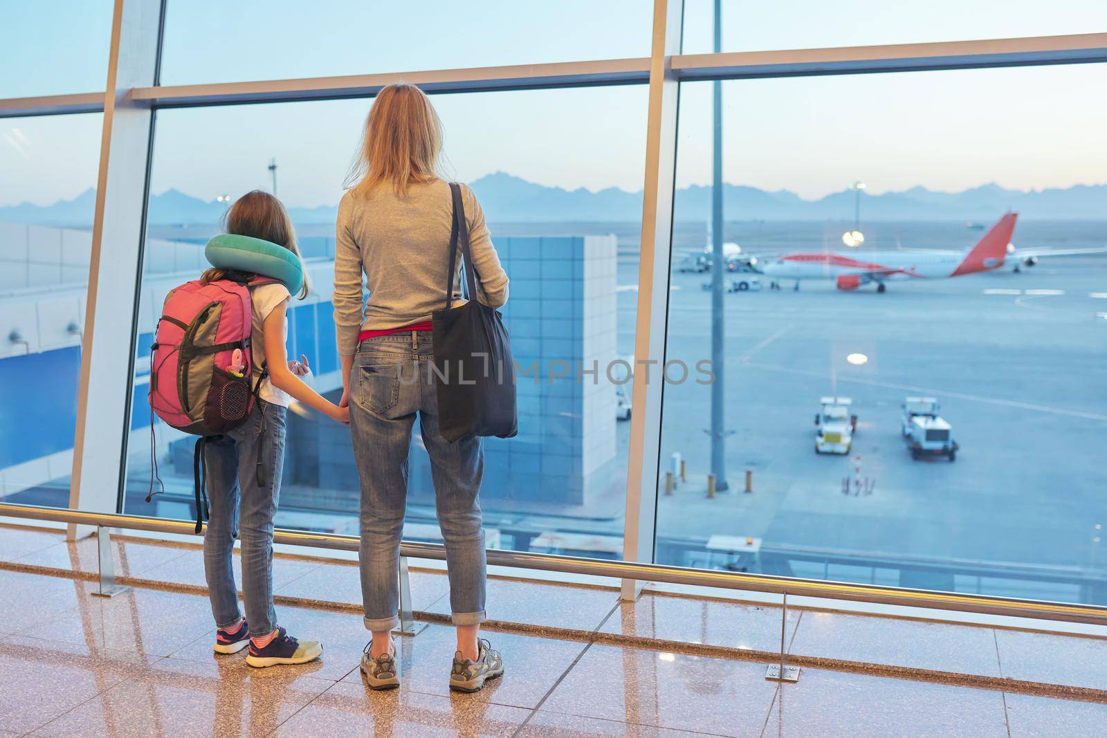Airport passengers family mother and daughter child looking at planes in panoramic window by VH-studio