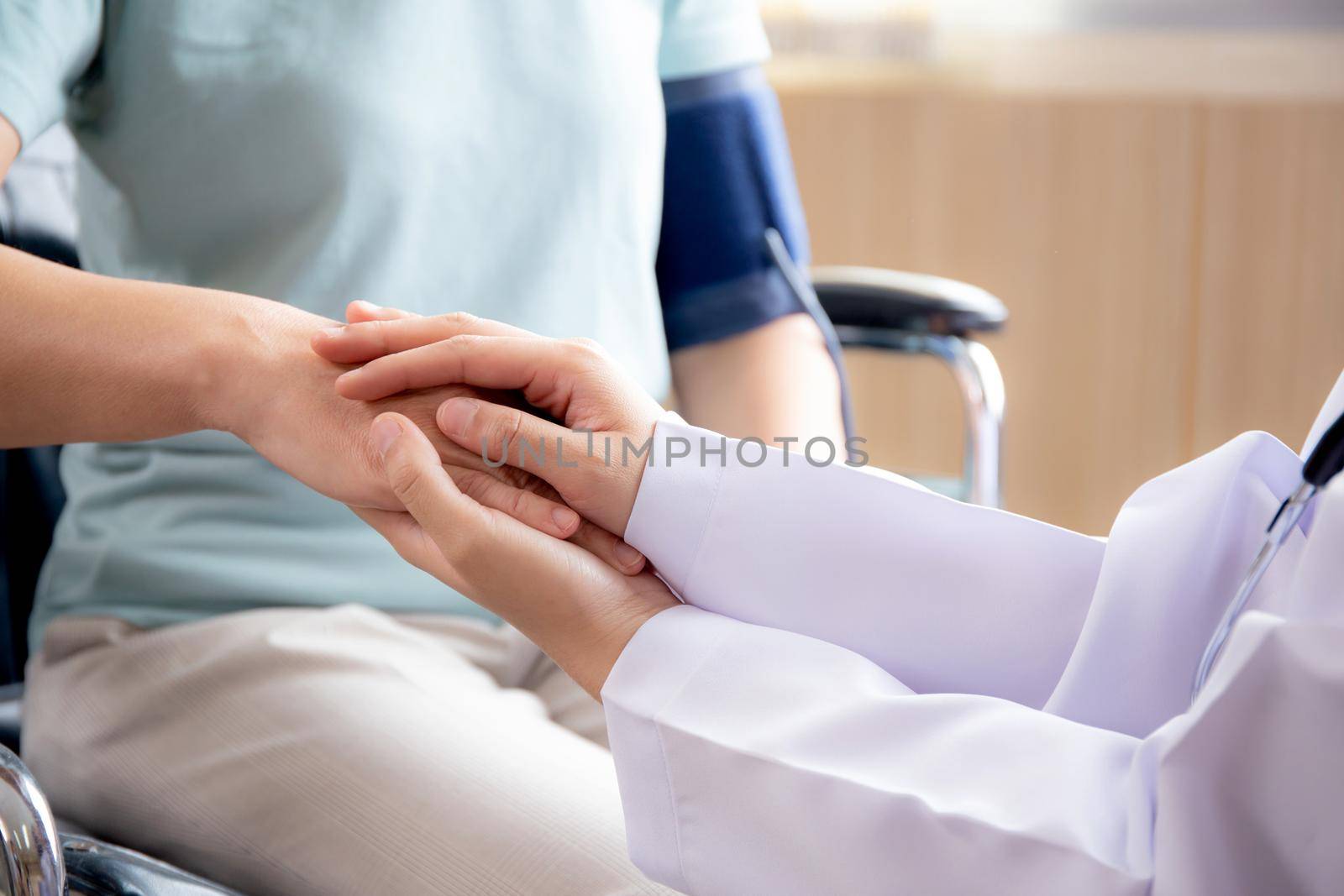 Closeup hands of doctor woman encourage patient senior sitting wheelchair at the hospital, physician take care and holding hands for consoling elderly, diagnostic disease and illness, medical concept.