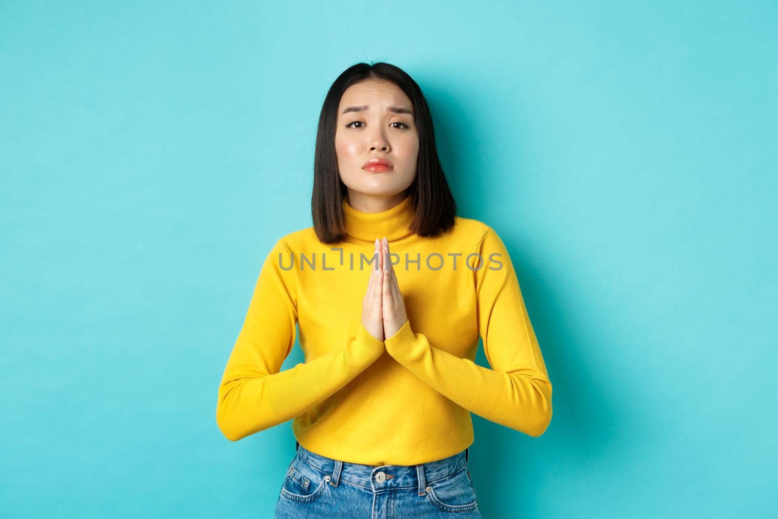 Young attractive asian girl begging for favour, need something and asking please, holding hands in pray, standing over blue background by Benzoix