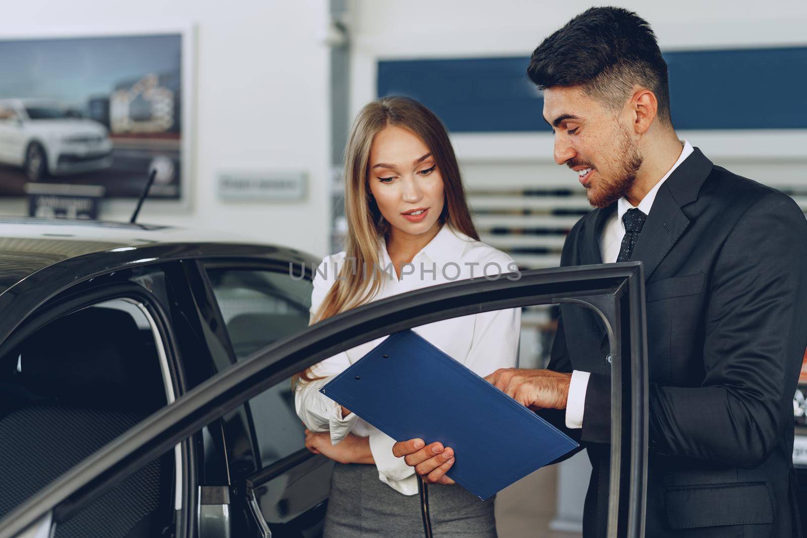 Man car dealer showing a woman buyer a new car in car salon