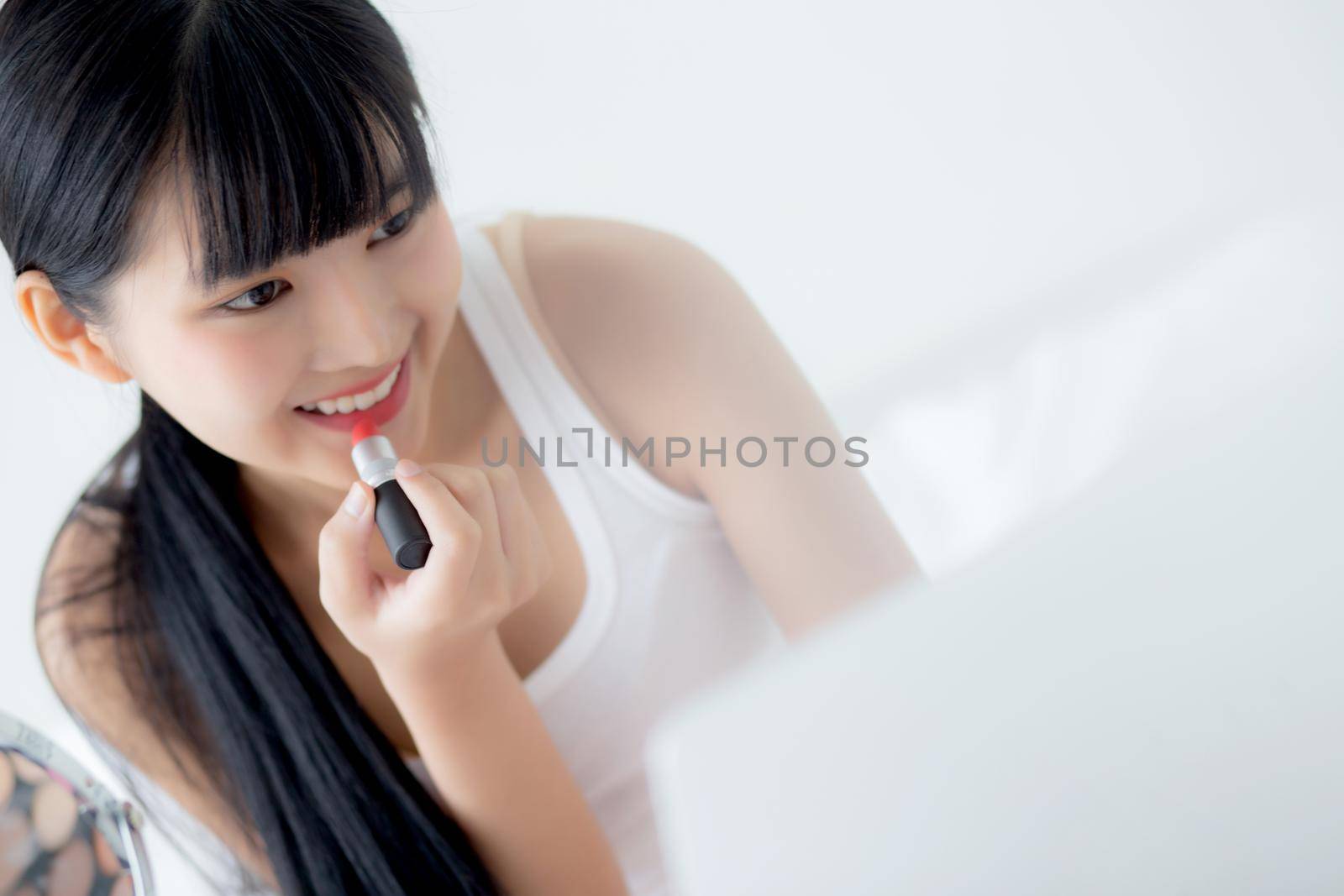 Beauty of young asian woman with learning makeup with lipstick on mouth watching laptop computer with tutorial course online on bed, female teaching and explain make up with cosmetic on streaming. by nnudoo