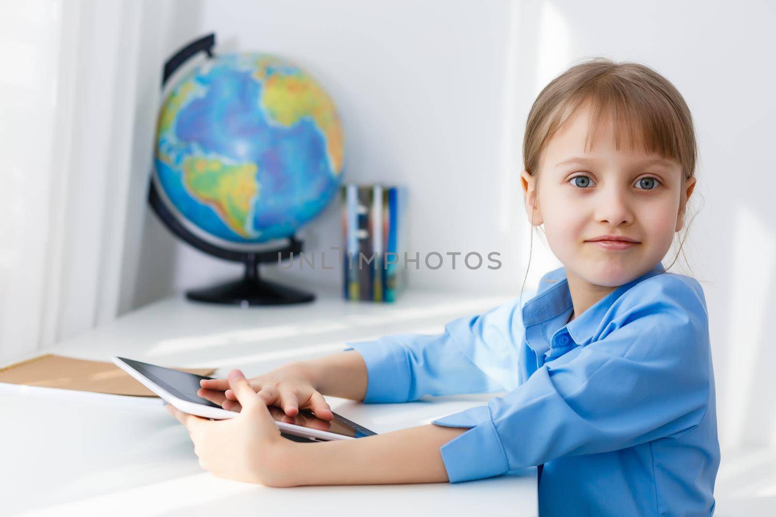 Smart little schoolgirl with digital tablet in a classroom. Child in an elementary school. Education and learning for kids.