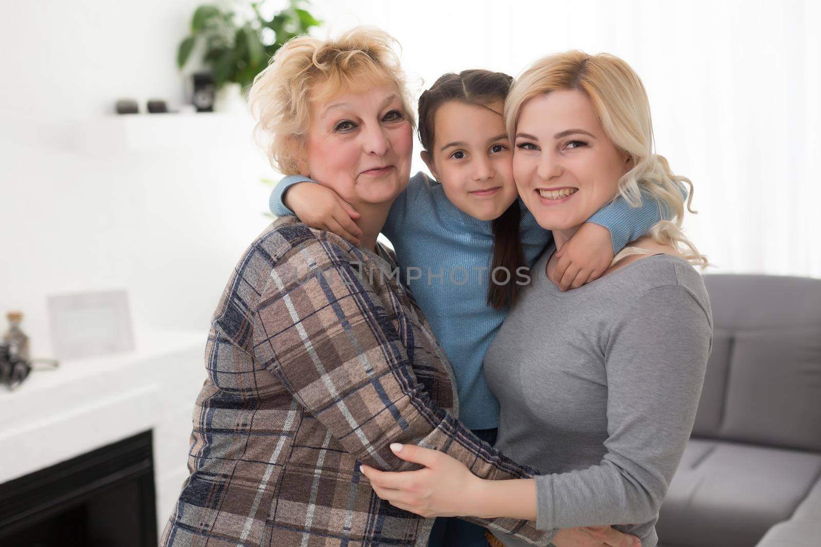 Three generations of women. Beautiful woman and teenage girl are kissing their granny while sitting on couch at home by Andelov13