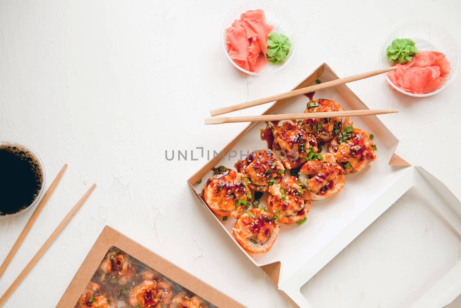 flat lay set with ginger and wasabi - baked sushi set with salmon in paper packaging on white background - bright delicious set of sushi rolls