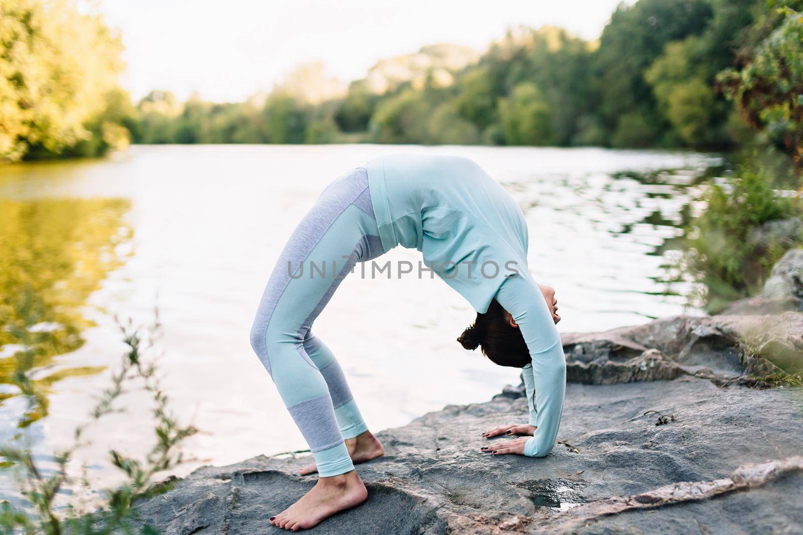 Pretty woman doing yoga exercises in the park on water background