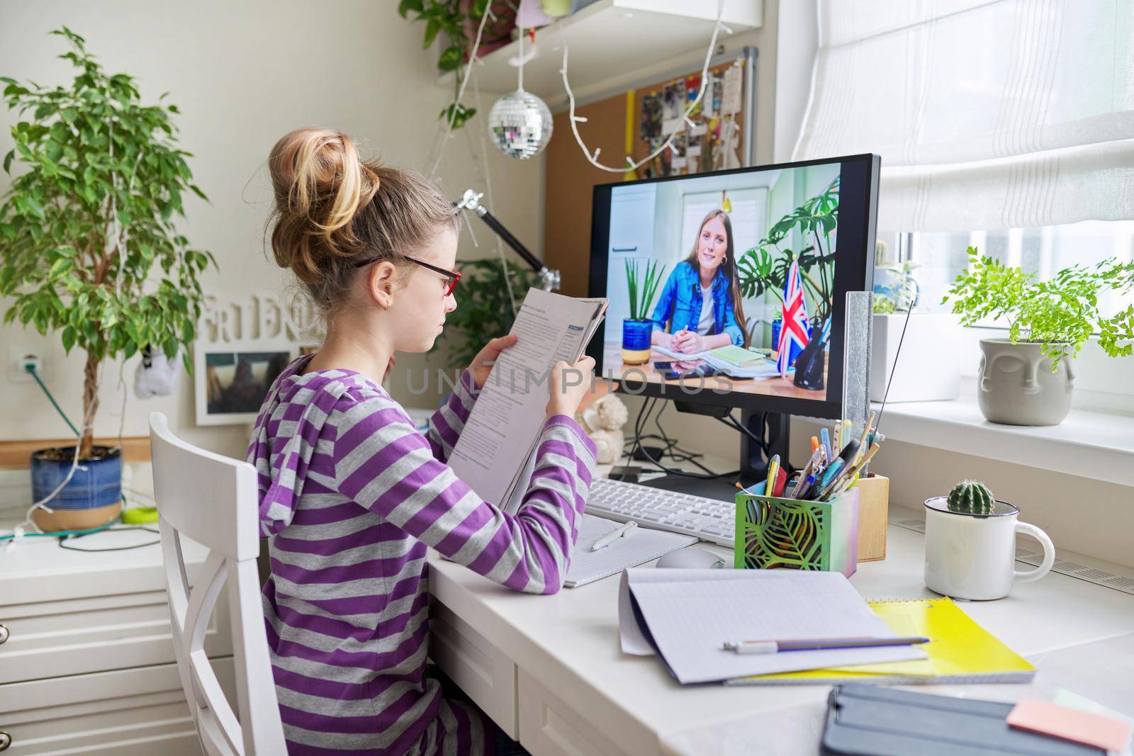 Learning English concept. Girl child at home studying language at home, online lesson, distance learning, e-education. Little student girl talking to teacher writing and reading