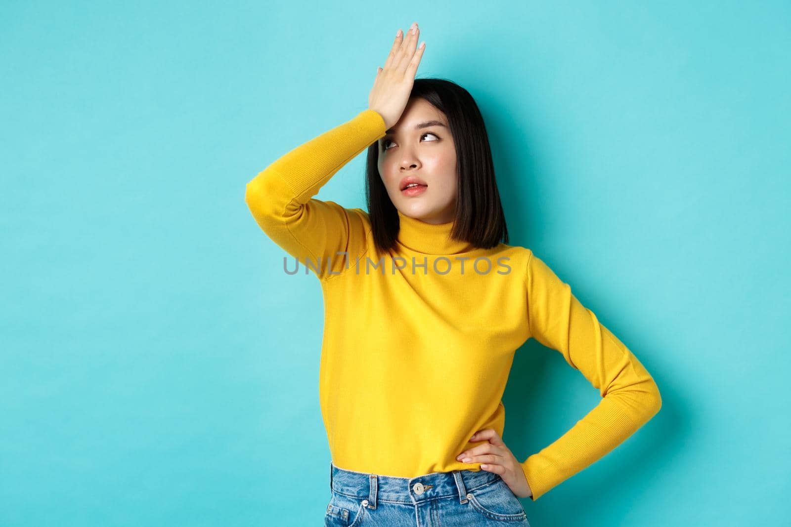 Emotions and lifestyle concept. Annoyed asian girl roll eyes and face palm, standing bothered in yellow pullover against blue background by Benzoix