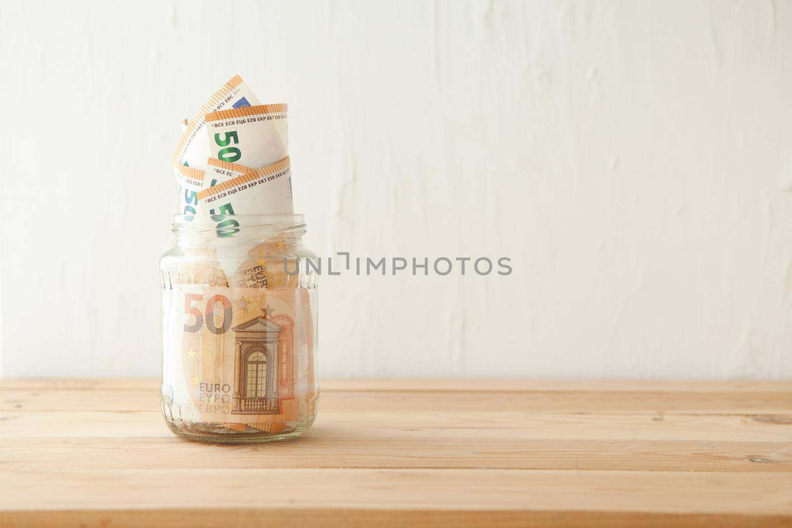 euro money banknotes in the glass jar at wooden table. Business concept. Money cash savings in glass pot at home.