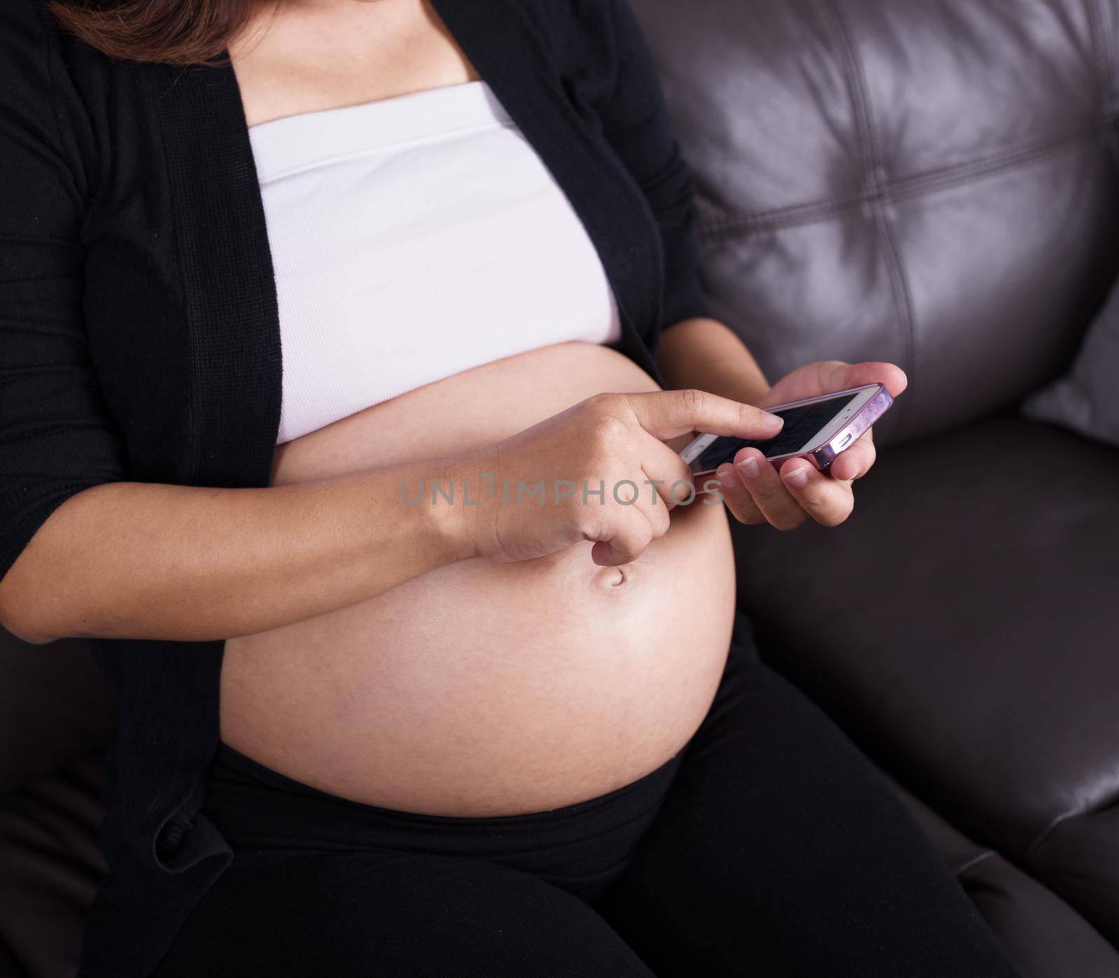 close up of pregnant woman using her mobile phone on sofa
