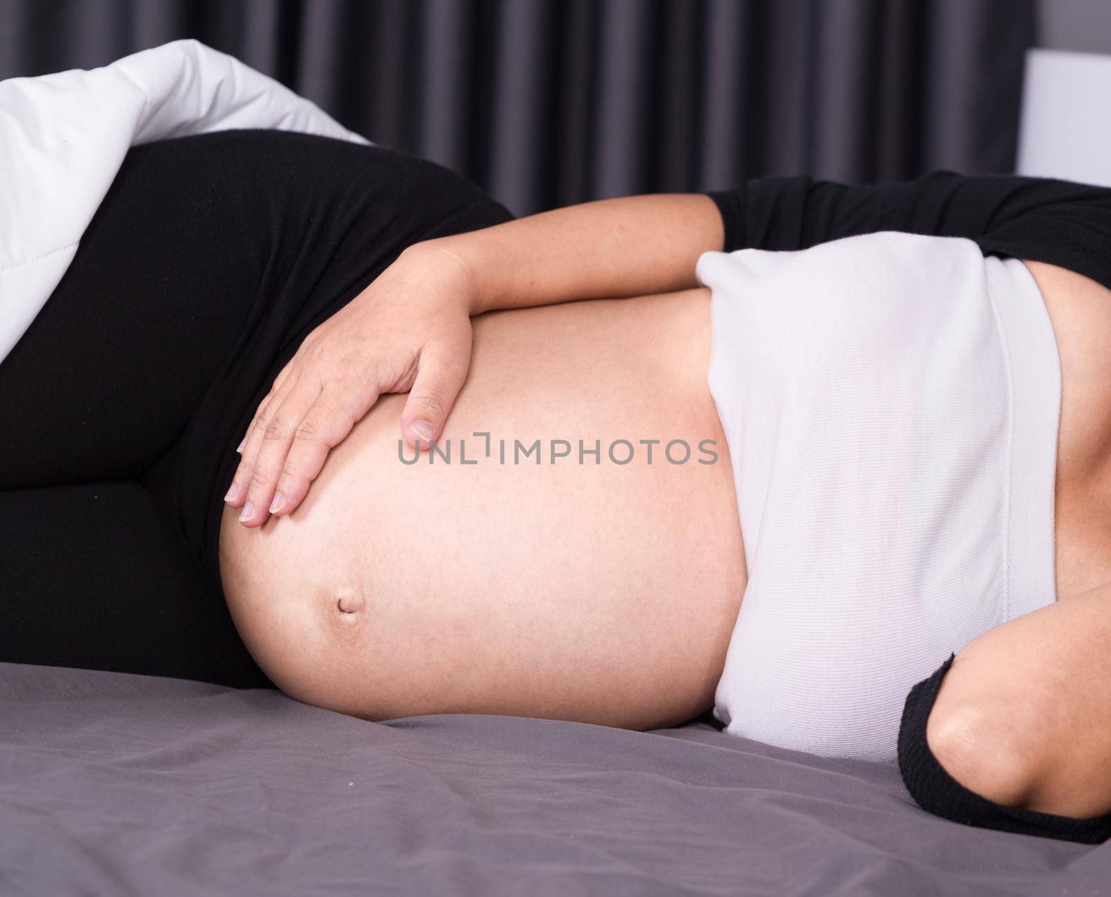 close up belly of pregnant woman sleeping on bed in the bedroom by geargodz