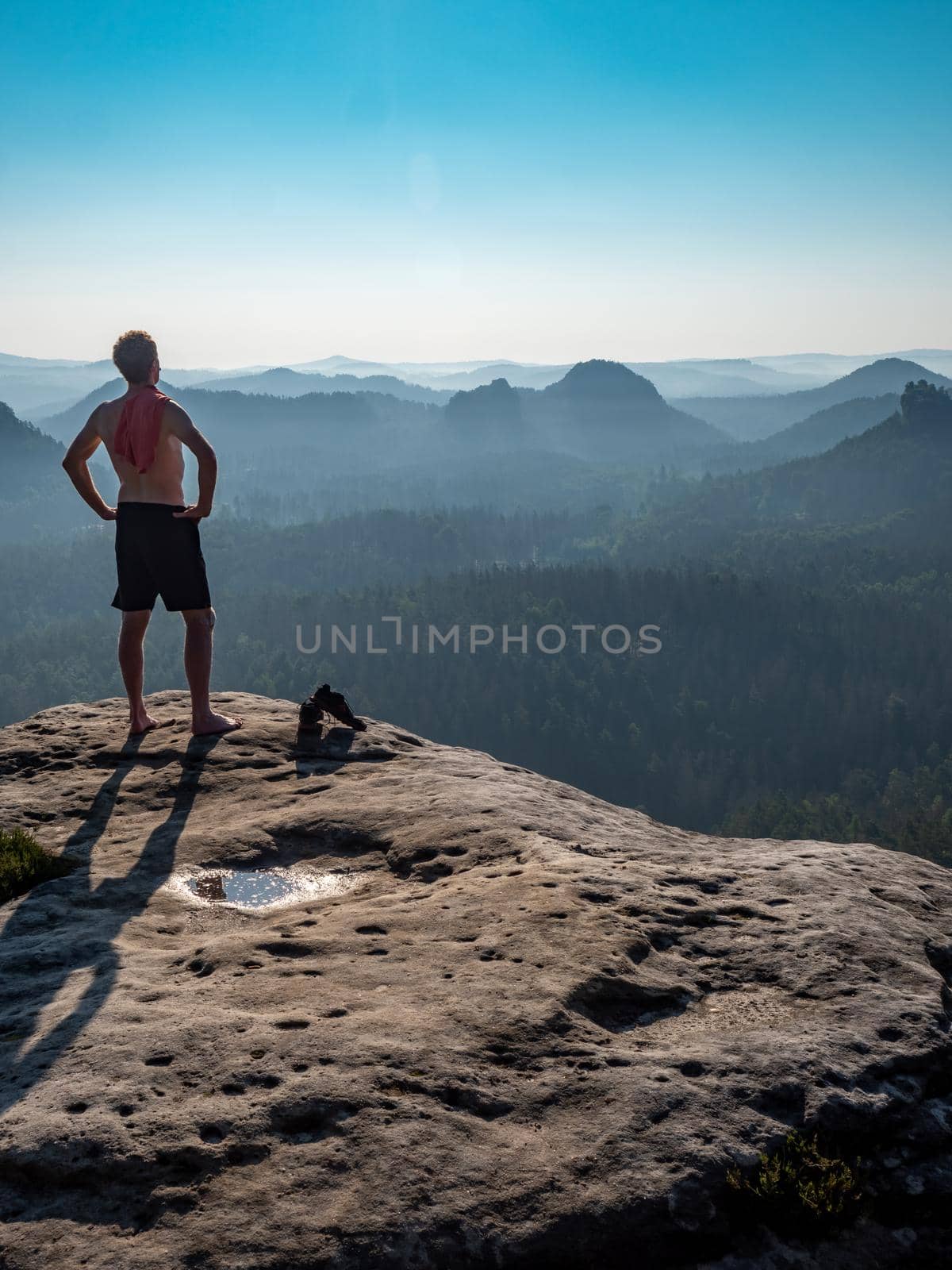 Naked man with a sporty figure on the edge of a rock enjoys the view of the morning landscape.