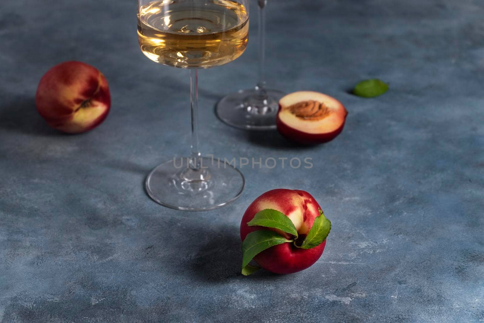 Several ripe peaches or nectarines and a glass of white peach wine sit on a blue plaster-textured surface. Wine drinking. Selective focus.