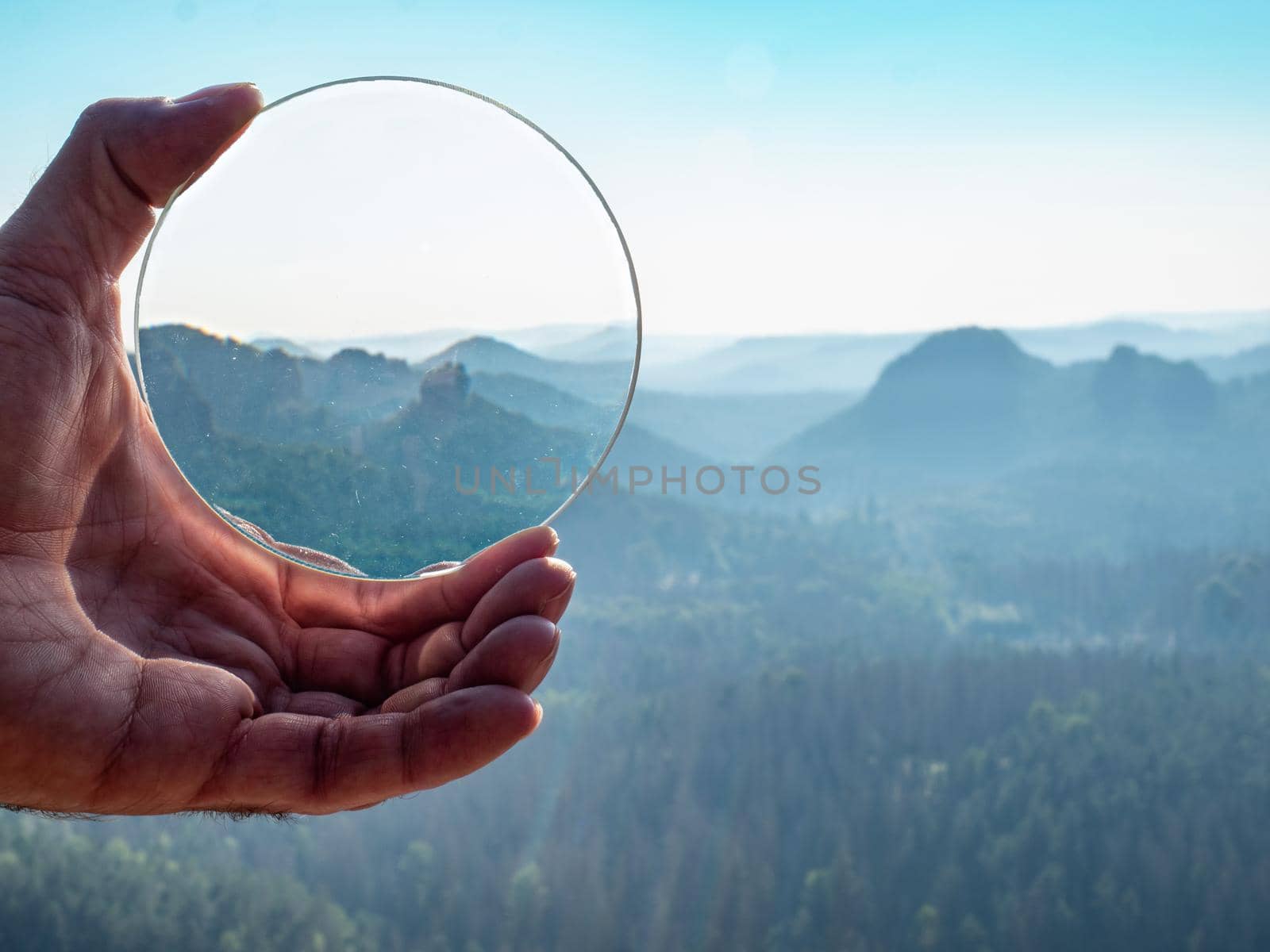 Crystal glass ball in a man's hand. The morning misty hilly landscape is reflected in the lens.