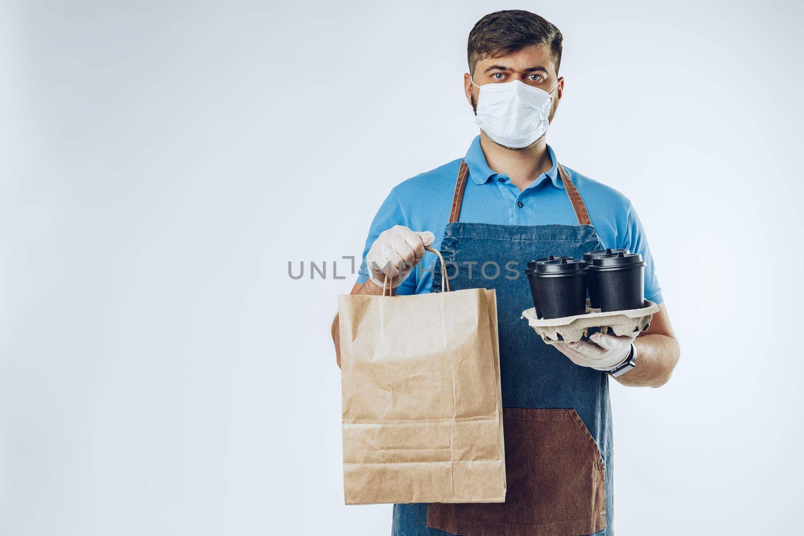 Delivery man in protective mask and medical gloves holding takeaway food. Compliance with the hygiene rules while covid-19 pandemic. Safe service