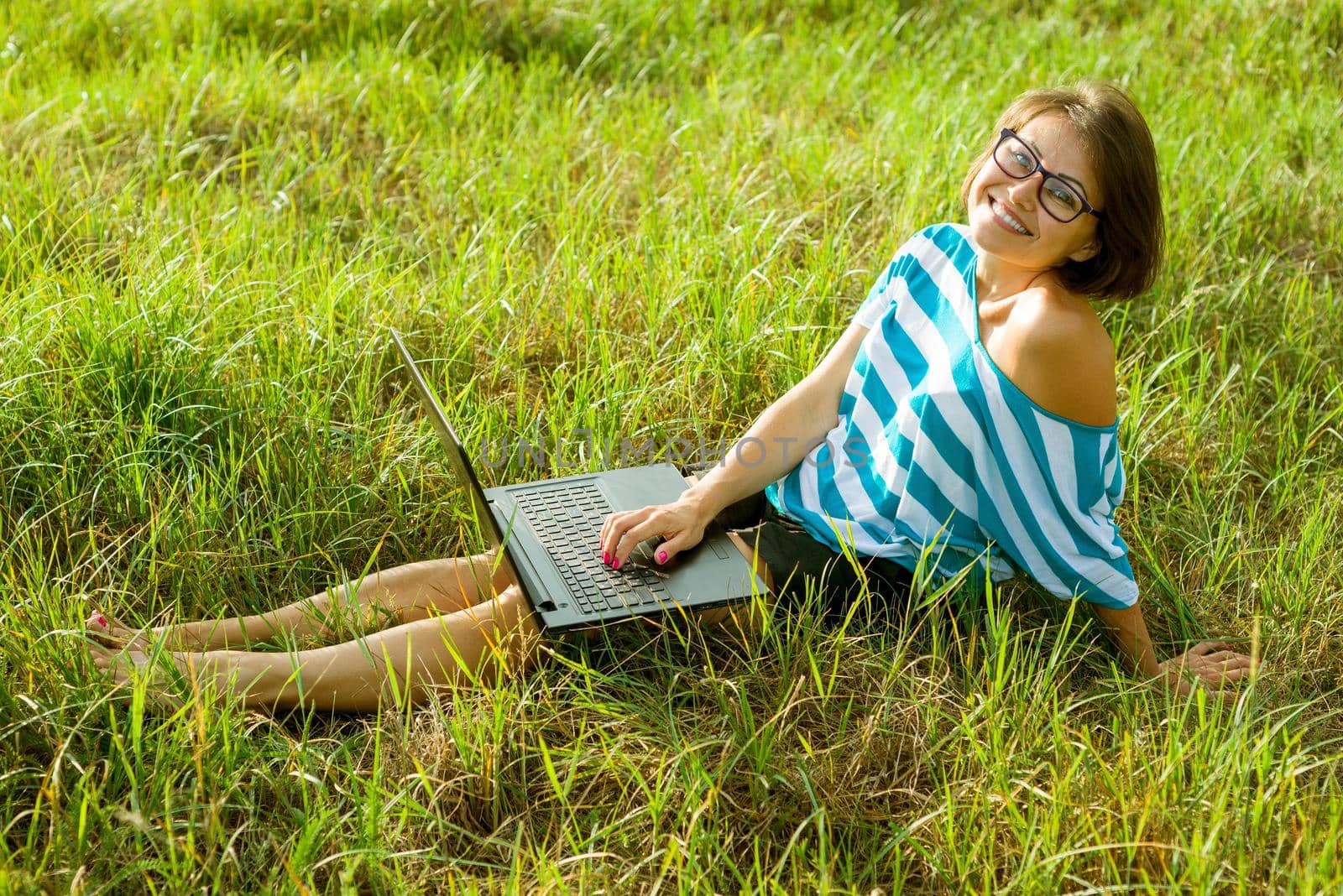 Beautiful woman freelancer working with laptop outdoors. Woman smiling sitting on the grass