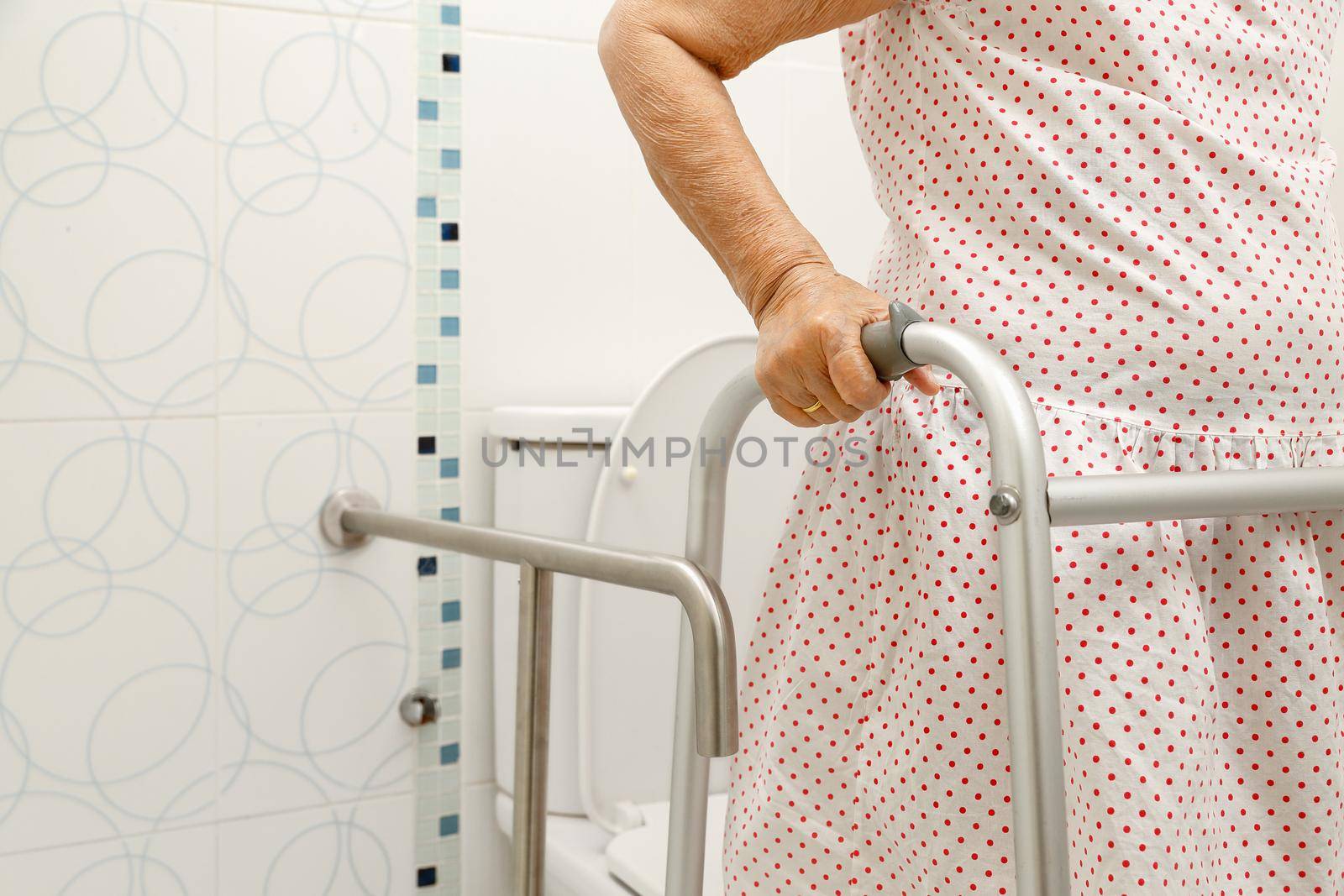 Elderly woman holding on handrail in toilet.