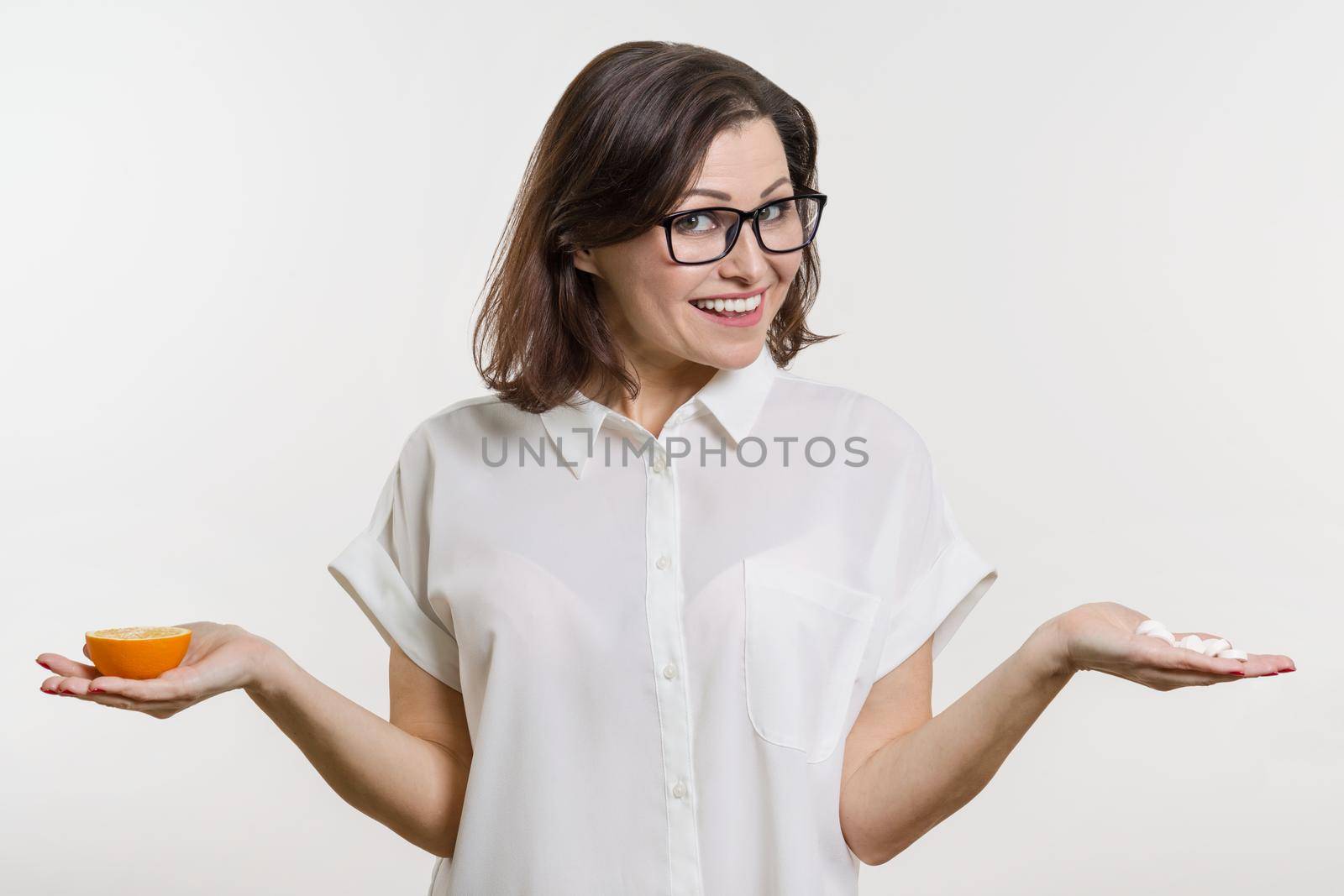 A woman holds a natural vitamin-orange in one hand and a synthetic vitamin C in the other. Makes a choice