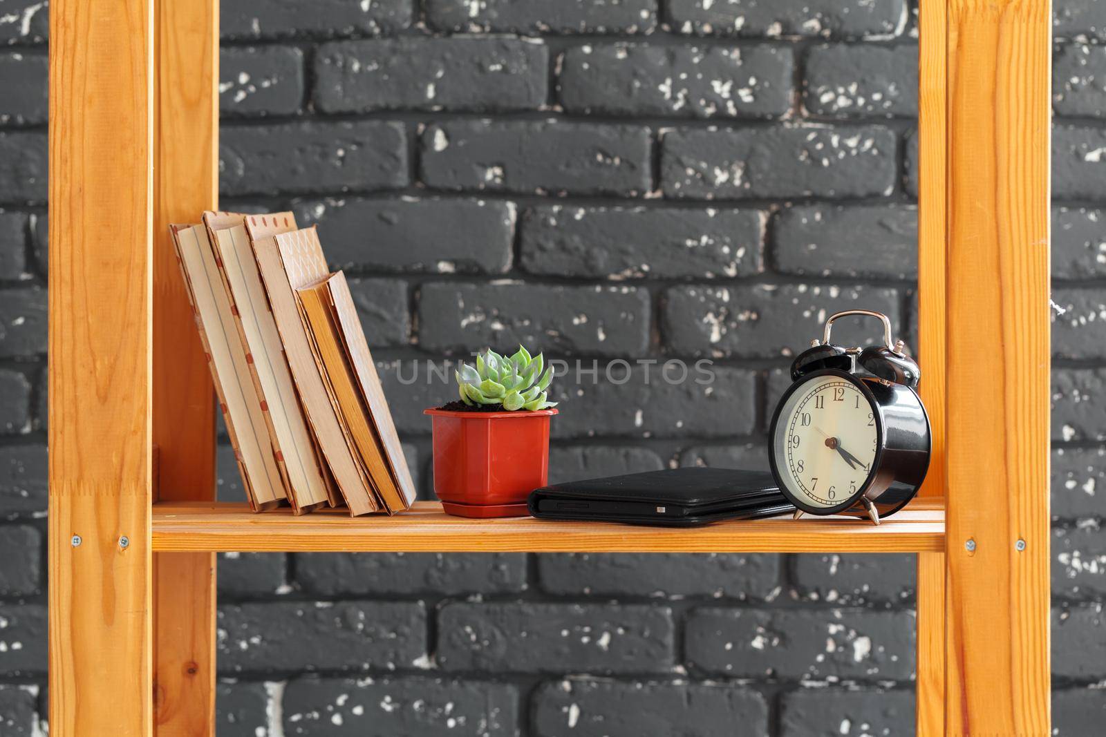 Wooden bookshelf with books and stuff against black brick wall. Close up.