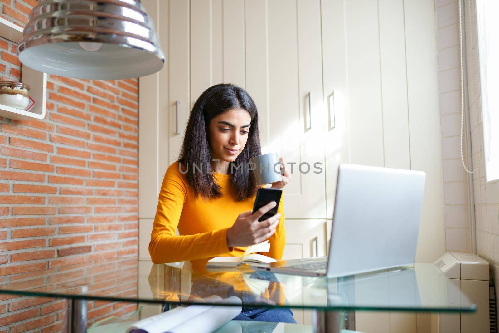 Female architect working at home with a laptop and blueprints. Persian woman. Persian woman with a coffee mug.