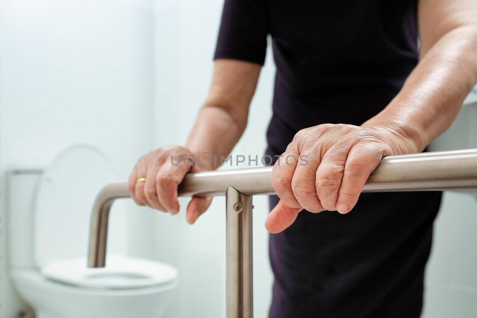 Elderly woman holding on handrail in bathroom.
