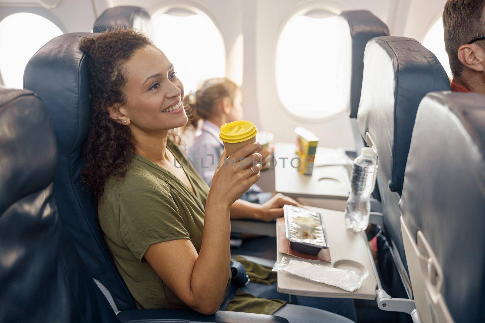 Happy female passenger drinking coffee and smiling while female flight attendant serving lunch on board by Yaroslav_astakhov