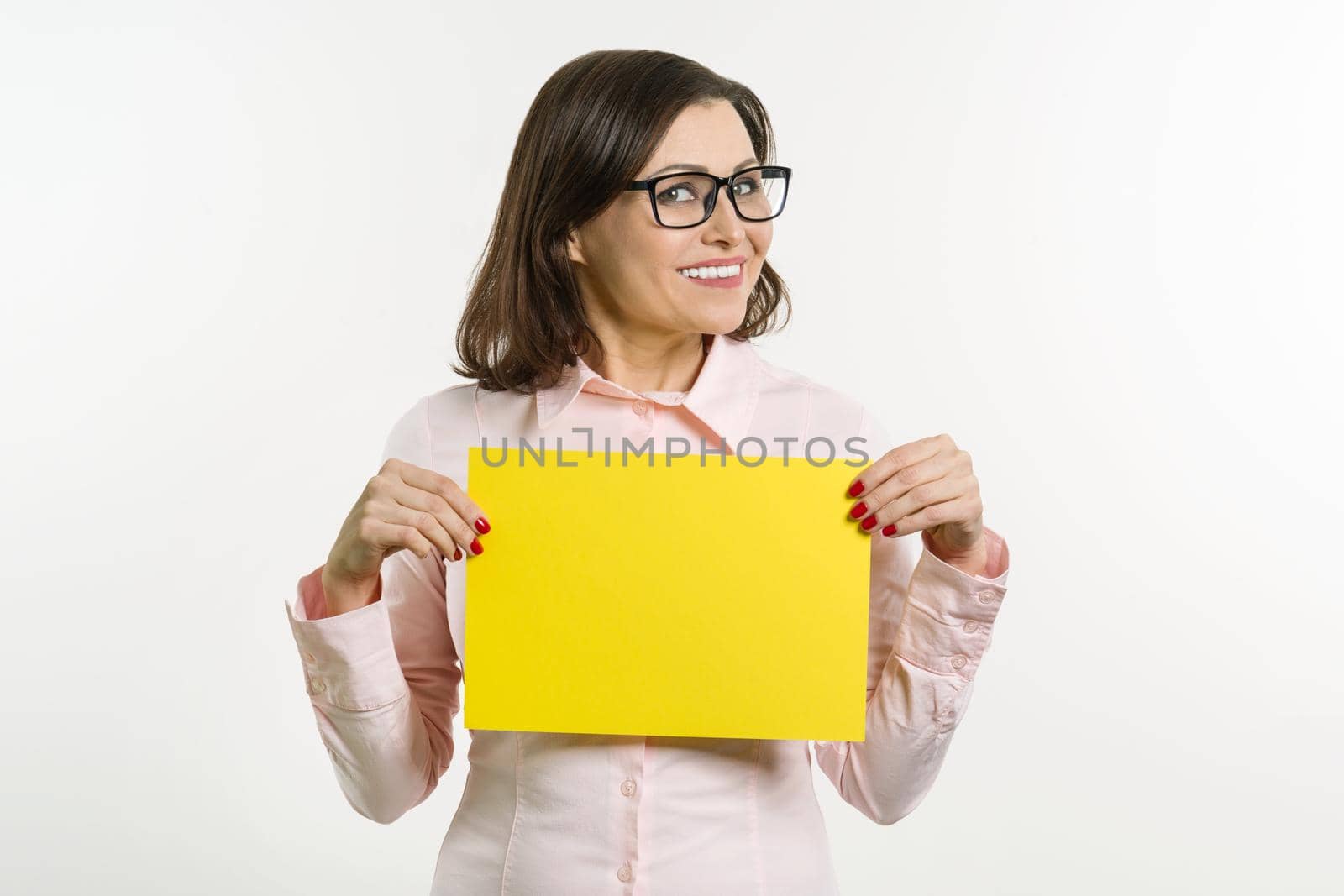 Smiling middle aged woman with yellow sheet of paper on white background.