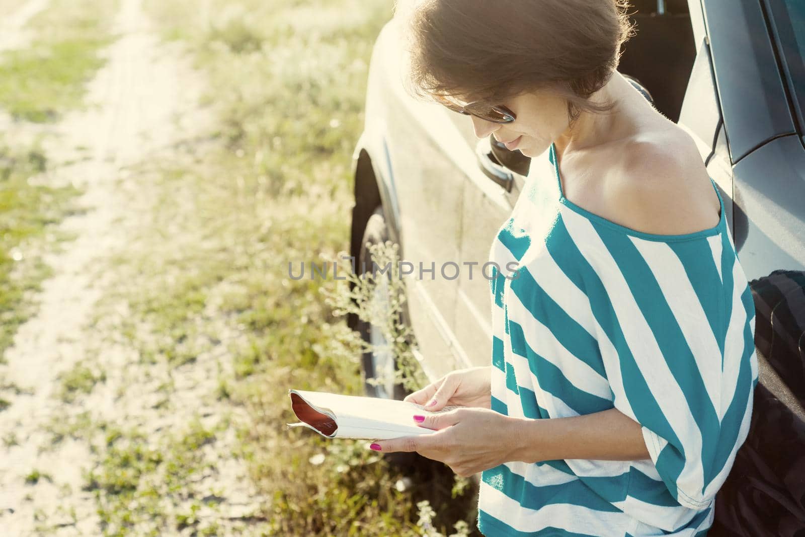 Beautiful adult woman is traveling. Stands on a country road with a road map near your car