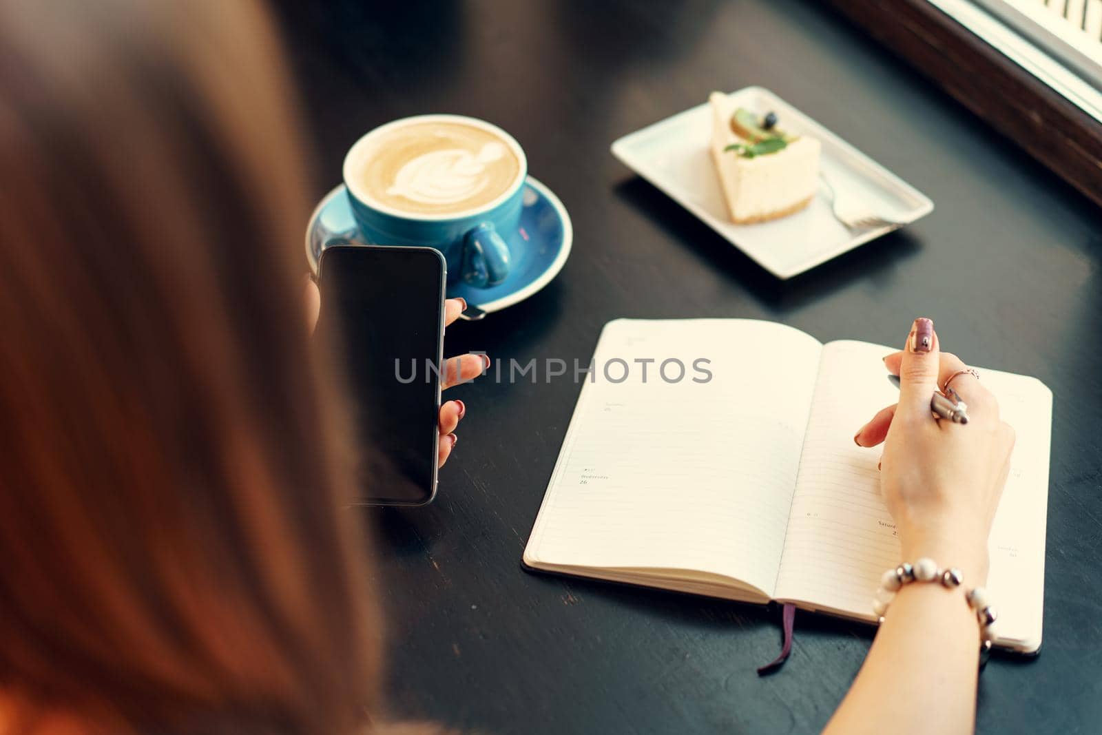 Young business woman sitting at the table in a coffee shop and making notes. Close up.