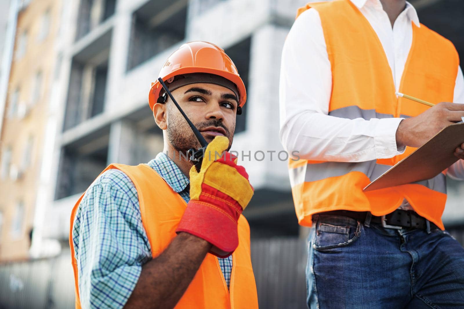 Young construction worker in uniform using walkie talkie on site, close up portrait