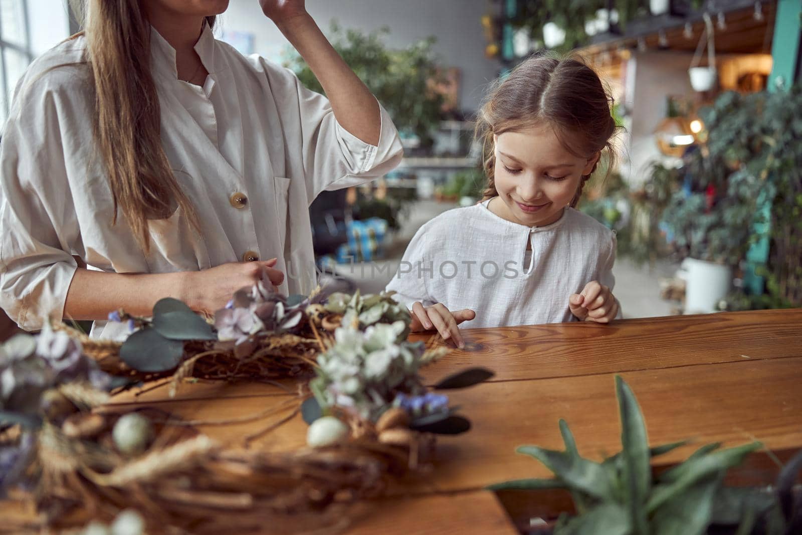 Flourist shop with different kinds of dryed flowers. Young happy confident specialist is working with her female kid.