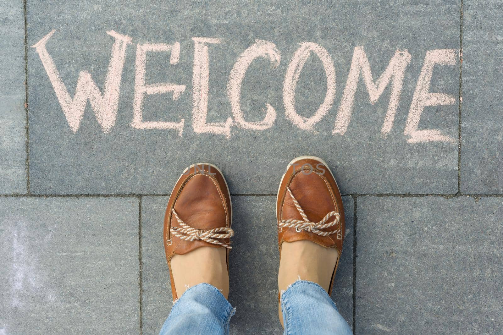 Female feet with text welcome written on grey sidewalk.