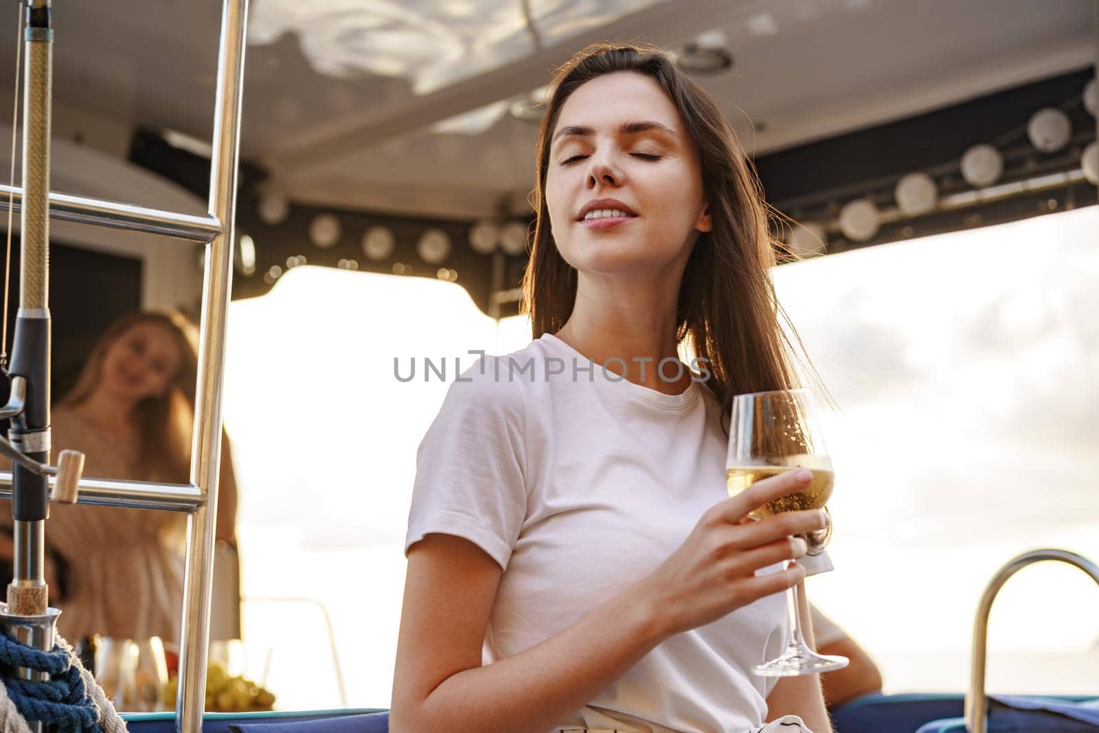 Young woman holding a wineglass and sitting on deck of sailing yacht boat