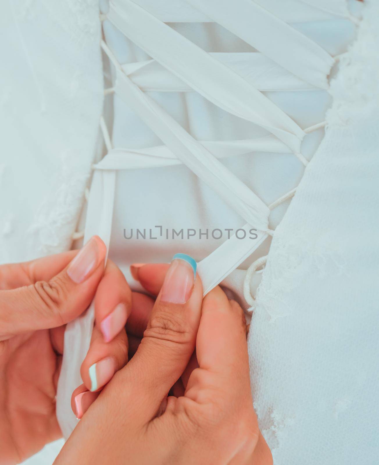 Morning preparation of the bride. Women's hands tie a ribbon on the corset of a wedding dress.