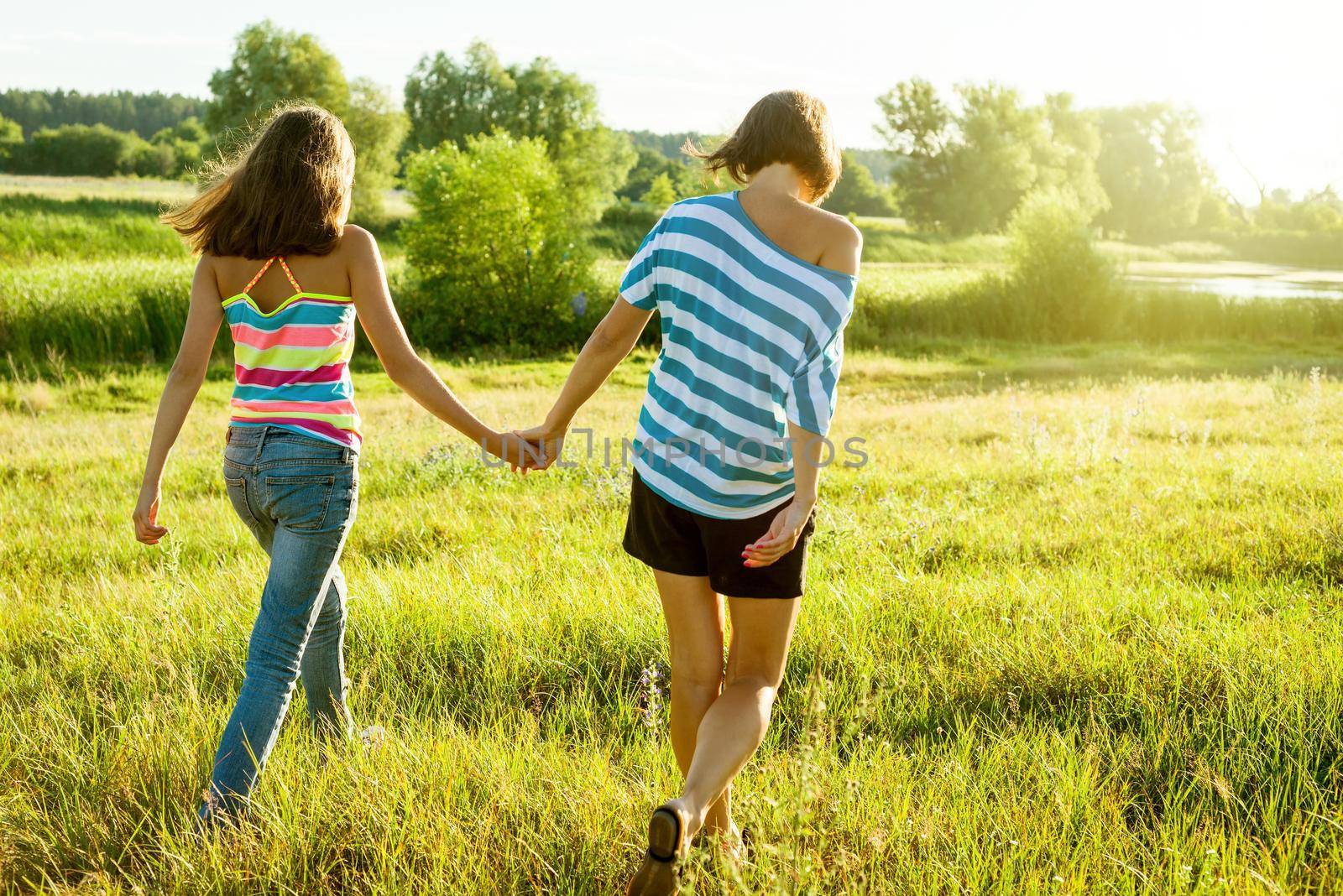 Mother and daughter holding hands, back view. Photo on nature in a sunny summer day.