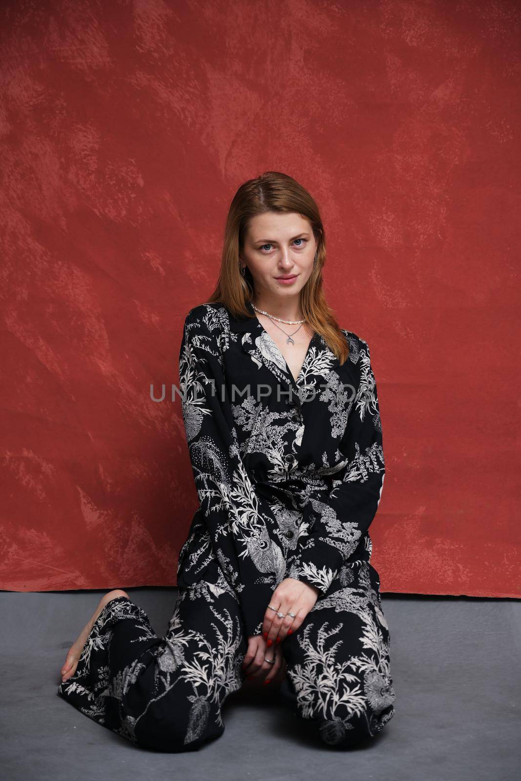 woman in dark clothes sits on the floor on a dark burgundy background